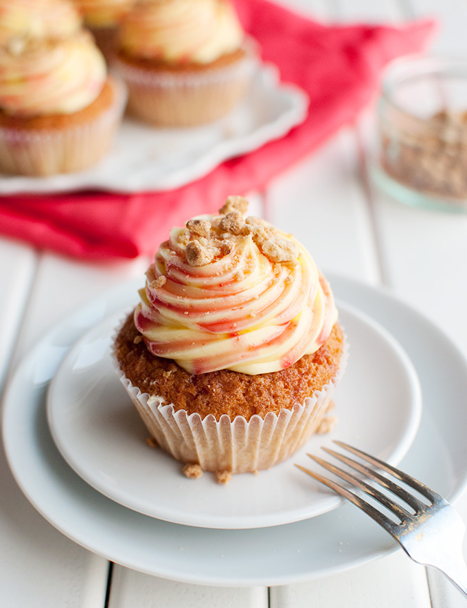 Rhubarb and Custard Cupcakes - These delicious cupcakes are filled with rhubarb puree and topped with a swirl of custard buttercream, rhubarb syrup, and crunchy crumb topping. Yum! | thetoughcookie.com